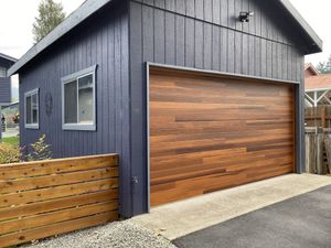 Blue shed with wooden garage door and small windows. Wooden fence and asphalt driveway.