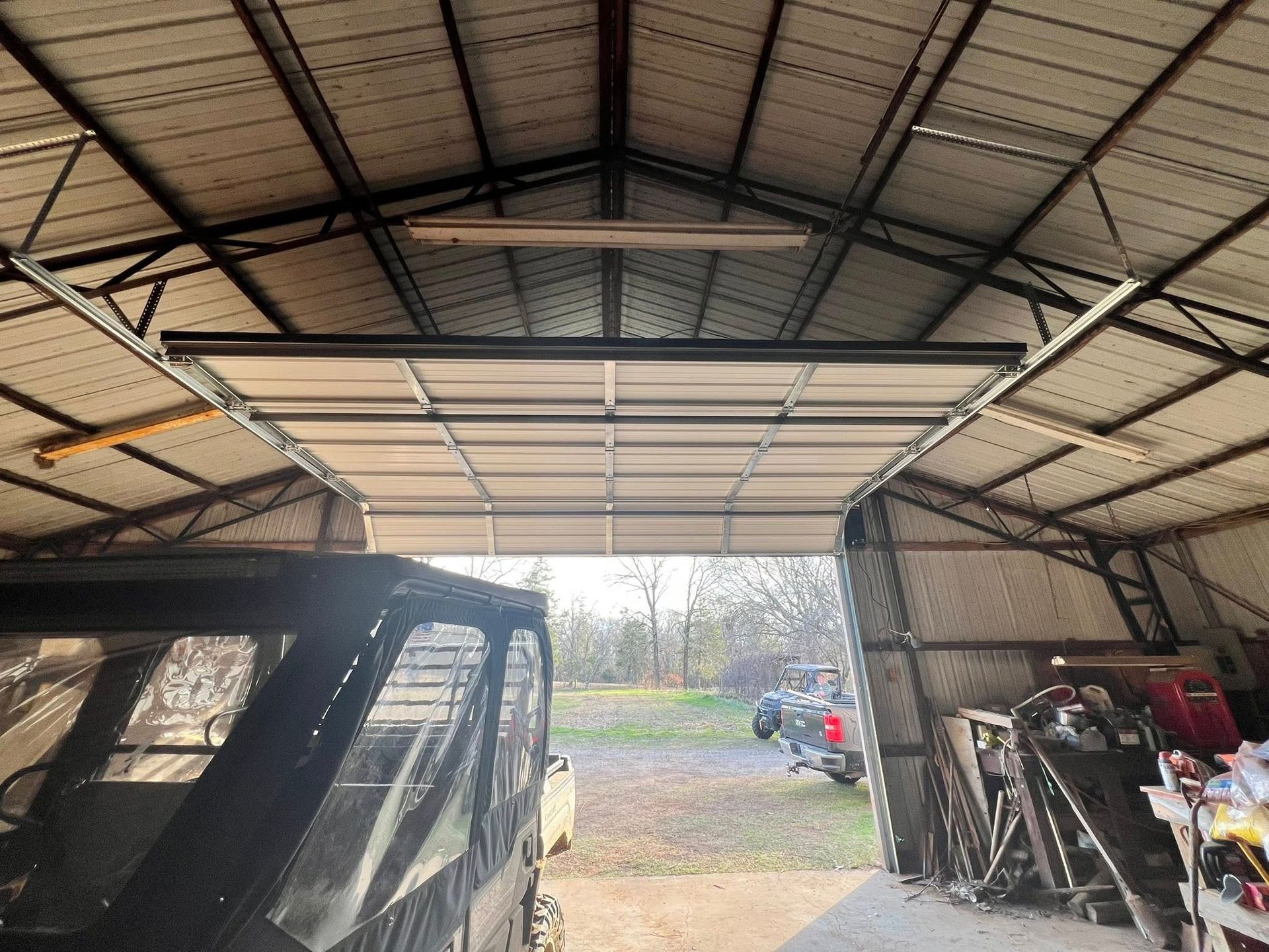 Garage interior with open door; vehicle inside, equipment on the right, light fixtures overhead.