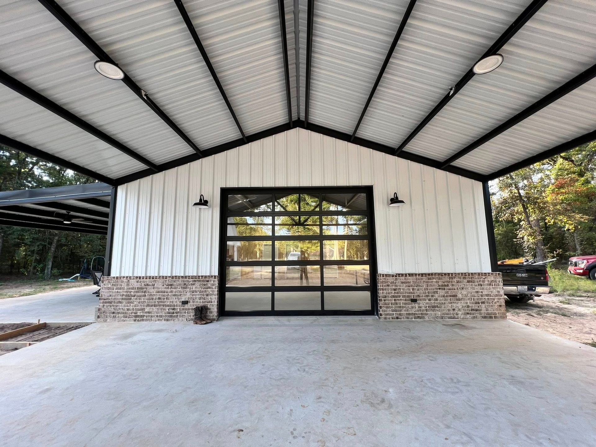 Open-air metal building with a large glass door, brick accents, and a concrete floor.