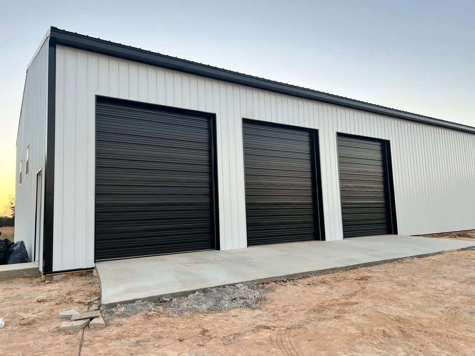 White industrial building with three black garage doors, on a concrete pad.