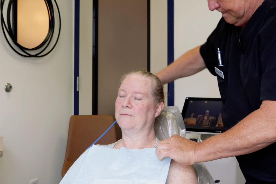 Woman reclining in a chair, head tilted back, wearing a red top in a clinical setting
