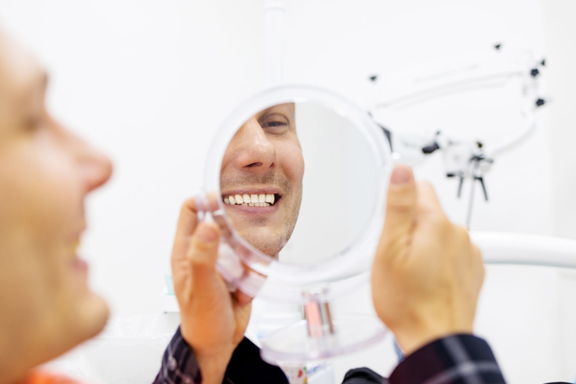 Patient viewing teeth in a dental mirror during a checkup, with a masked dentist nearby