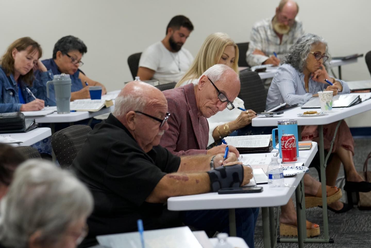 People seated at desks, writing during a class or meeting. Inside, neutral colors.