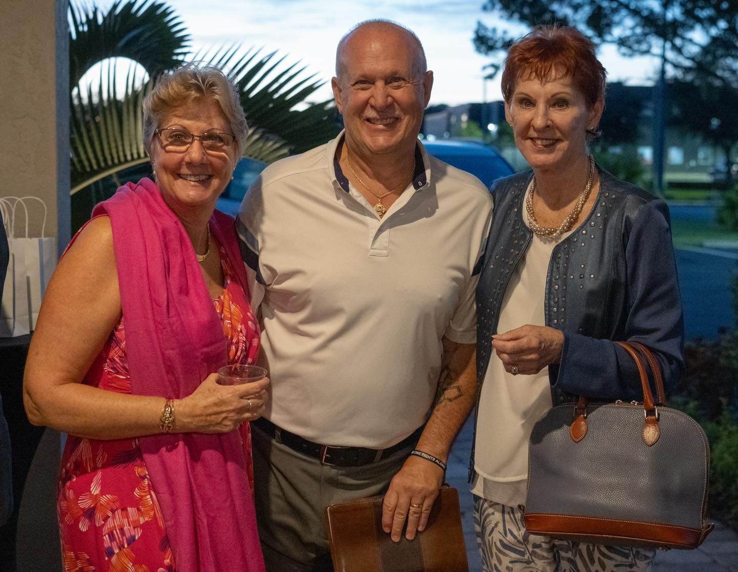 Three people smiling, posing outdoors.Two women and one man.