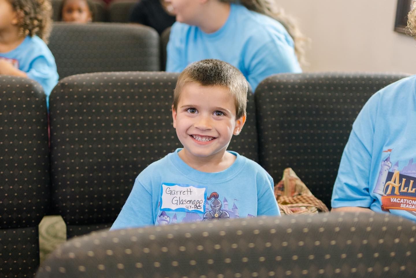 Boy in a blue shirt smiles at the camera, seated in a church pew.