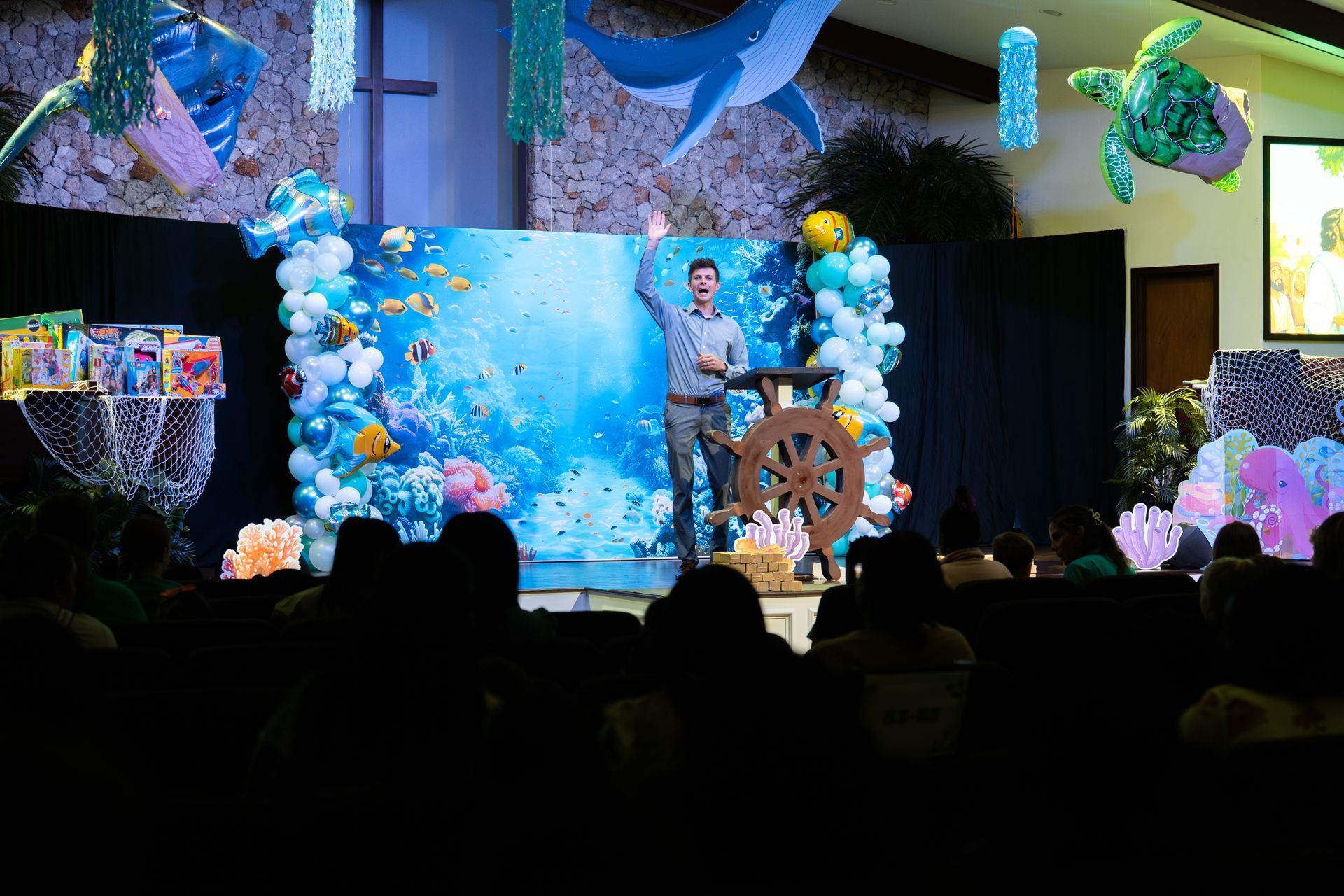 A man speaks to a crowd in a church decorated for a medieval-themed event.