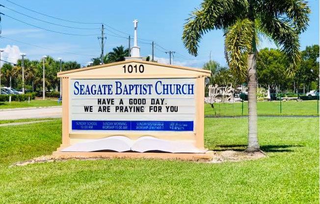 Sign for Seagate Baptist Church, says “Have a good day, We are praying for you” outdoors on a sunny day.