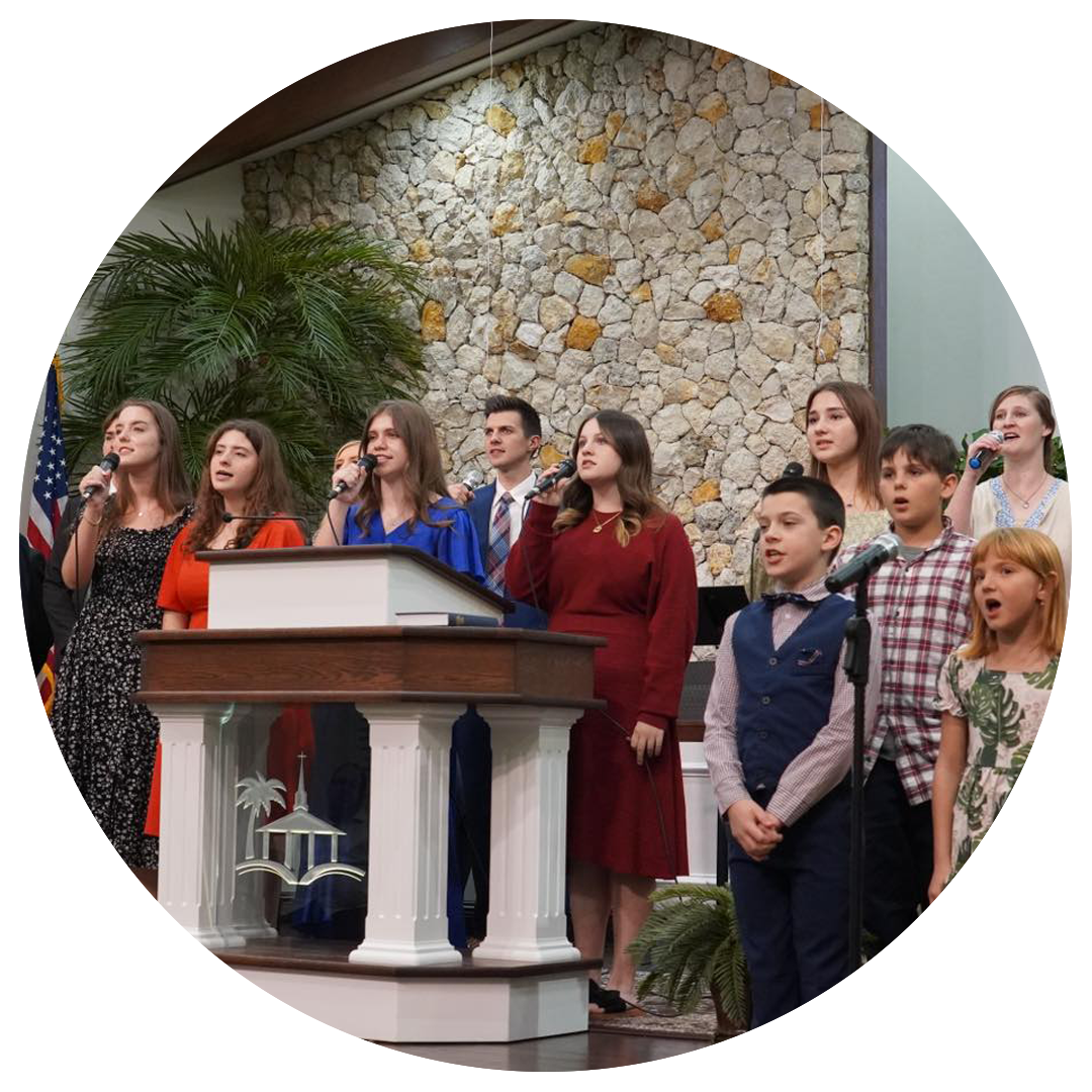 Choir singing at a podium. Various ages, dressed in formal wear, stand in front of a stone wall.