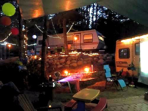 A rv parked next to a picnic table and chairs at night.