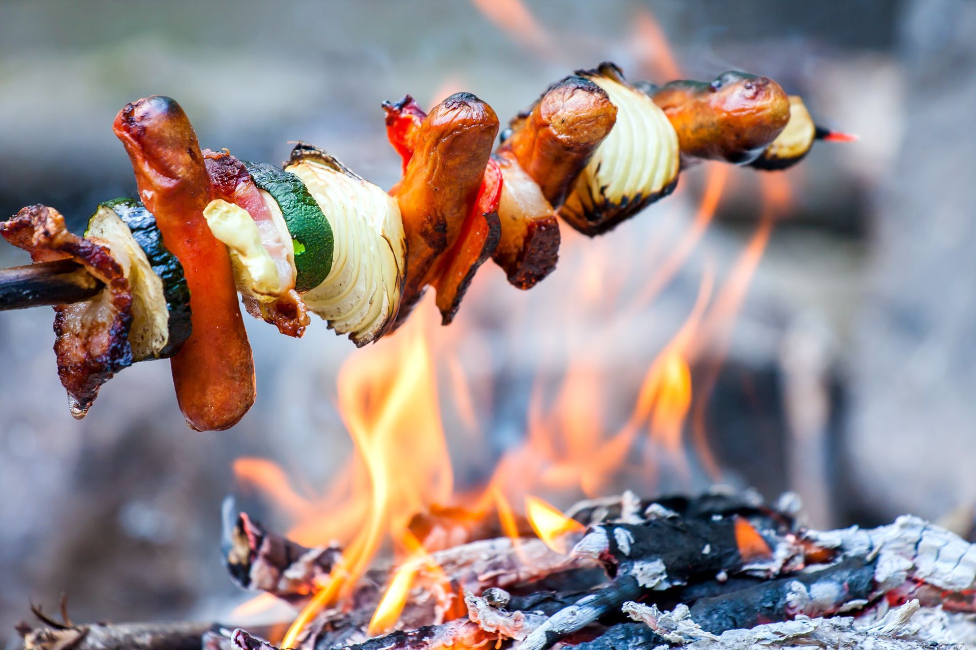 A skewer of meat and vegetables is cooking over a fire.
