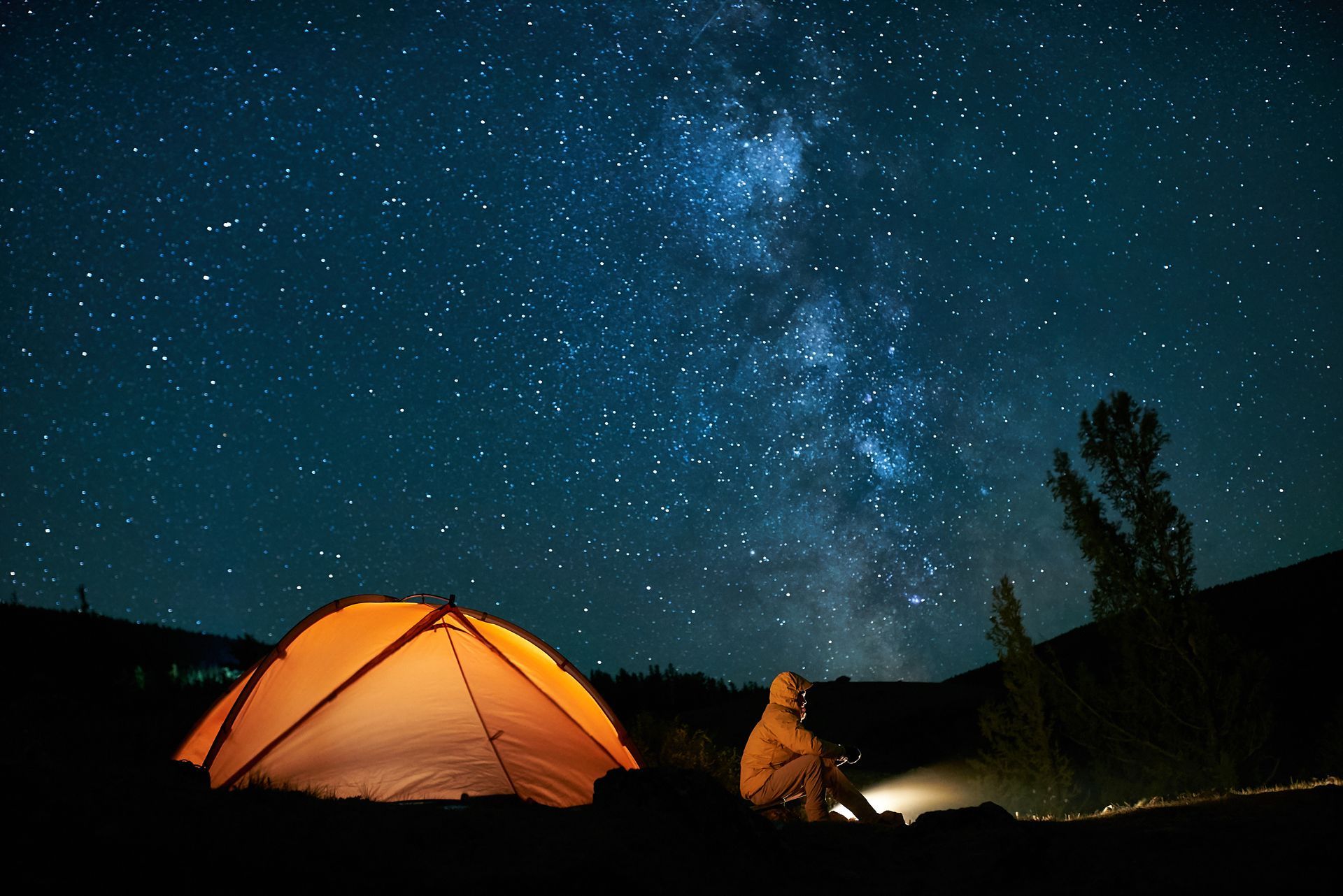 A person is sitting in front of a tent under a starry night sky