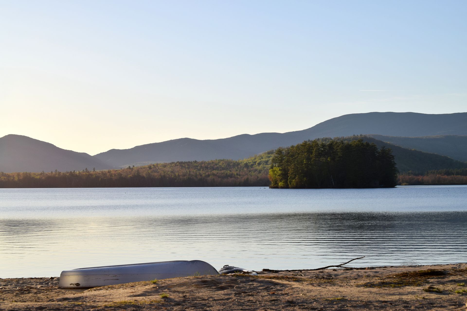 A boat is sitting on the shore of a lake with mountains in the background.