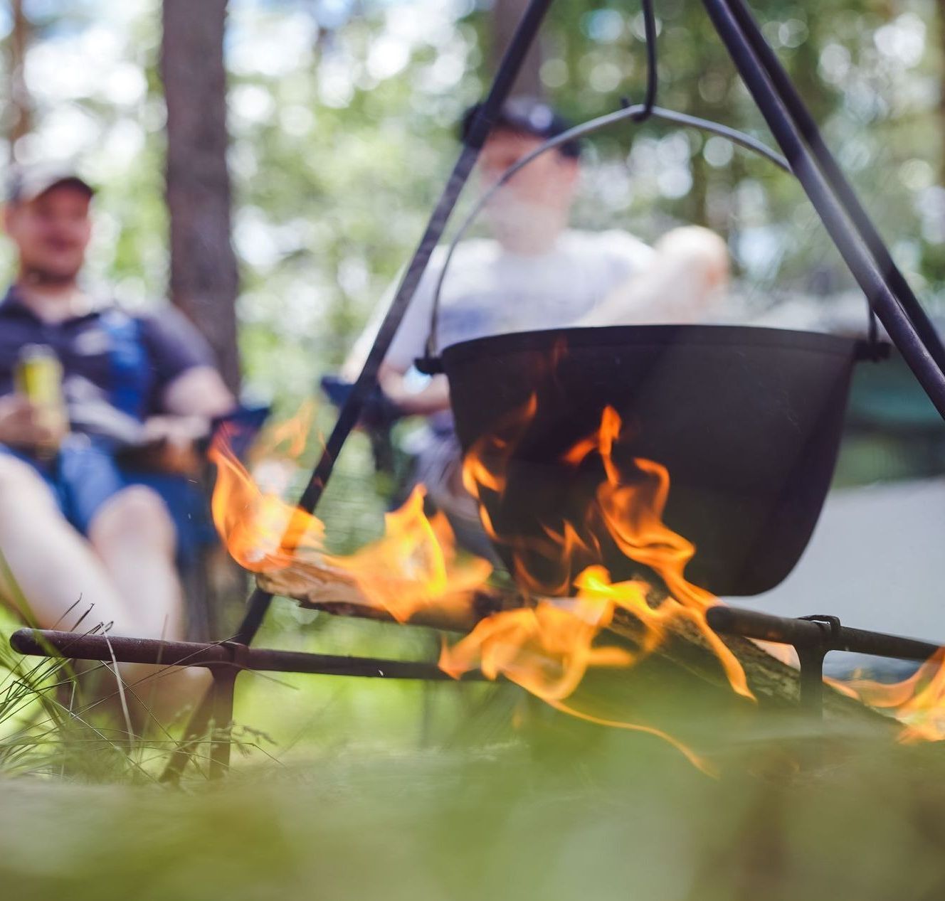 A group of people are sitting around a campfire with a pot on it.