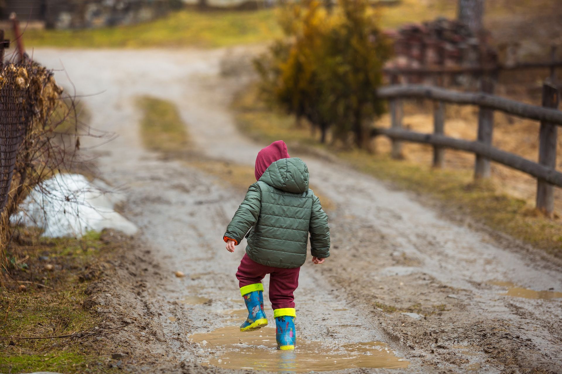 A little boy wearing rain boots is walking down a muddy road.