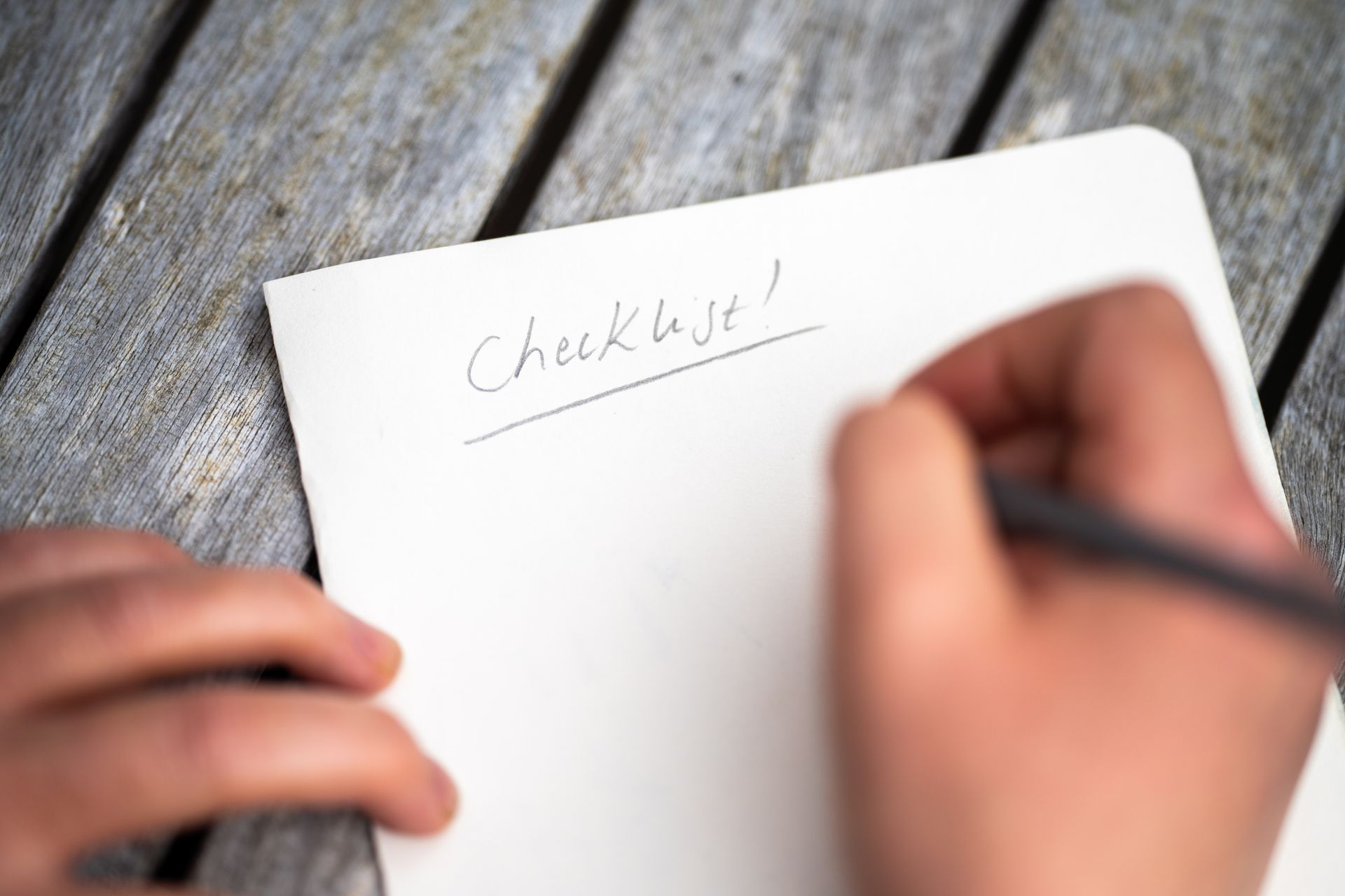 A person is writing on a piece of paper that says checklist
