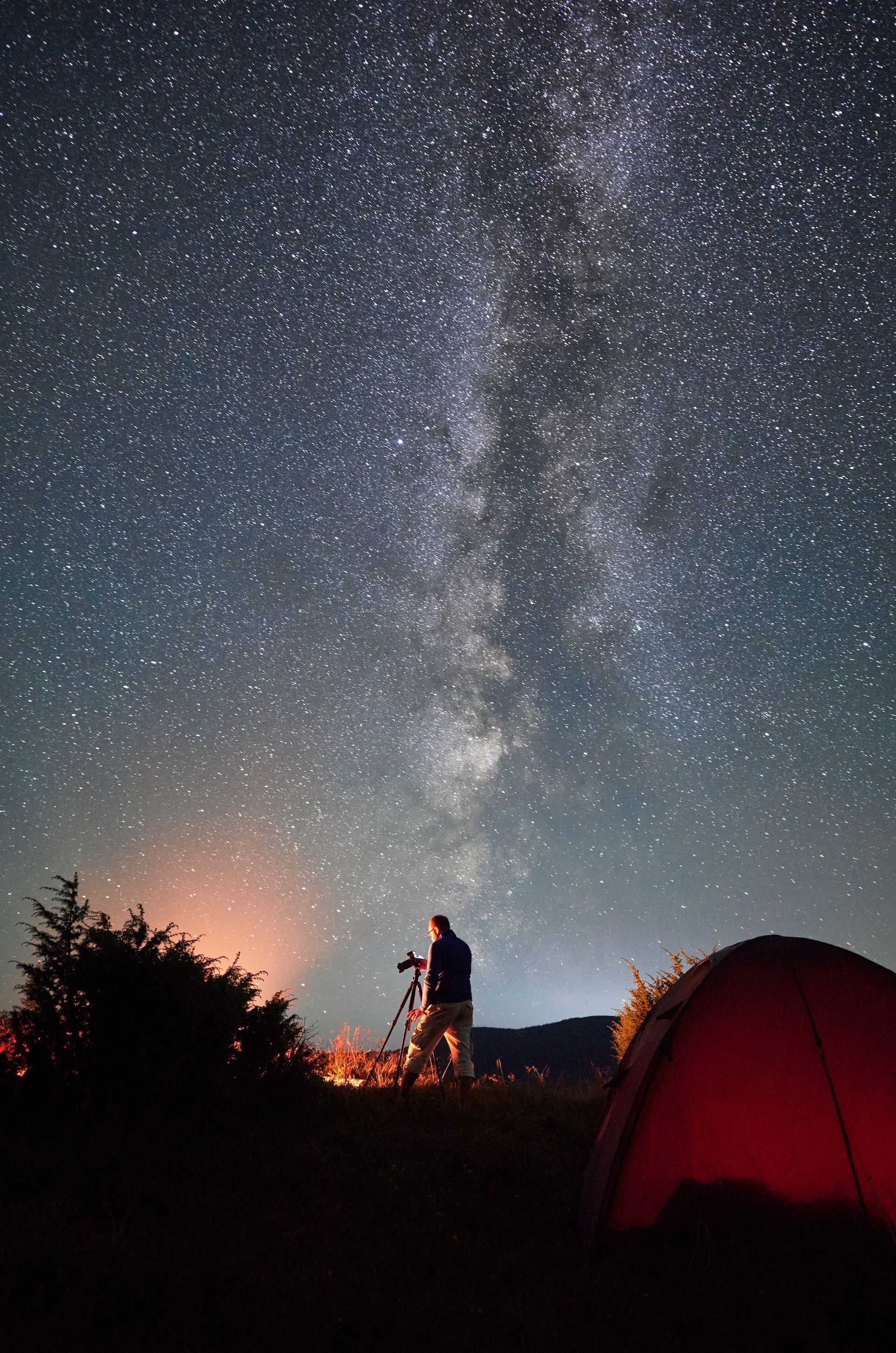 A man is standing in front of a tent under a starry night sky