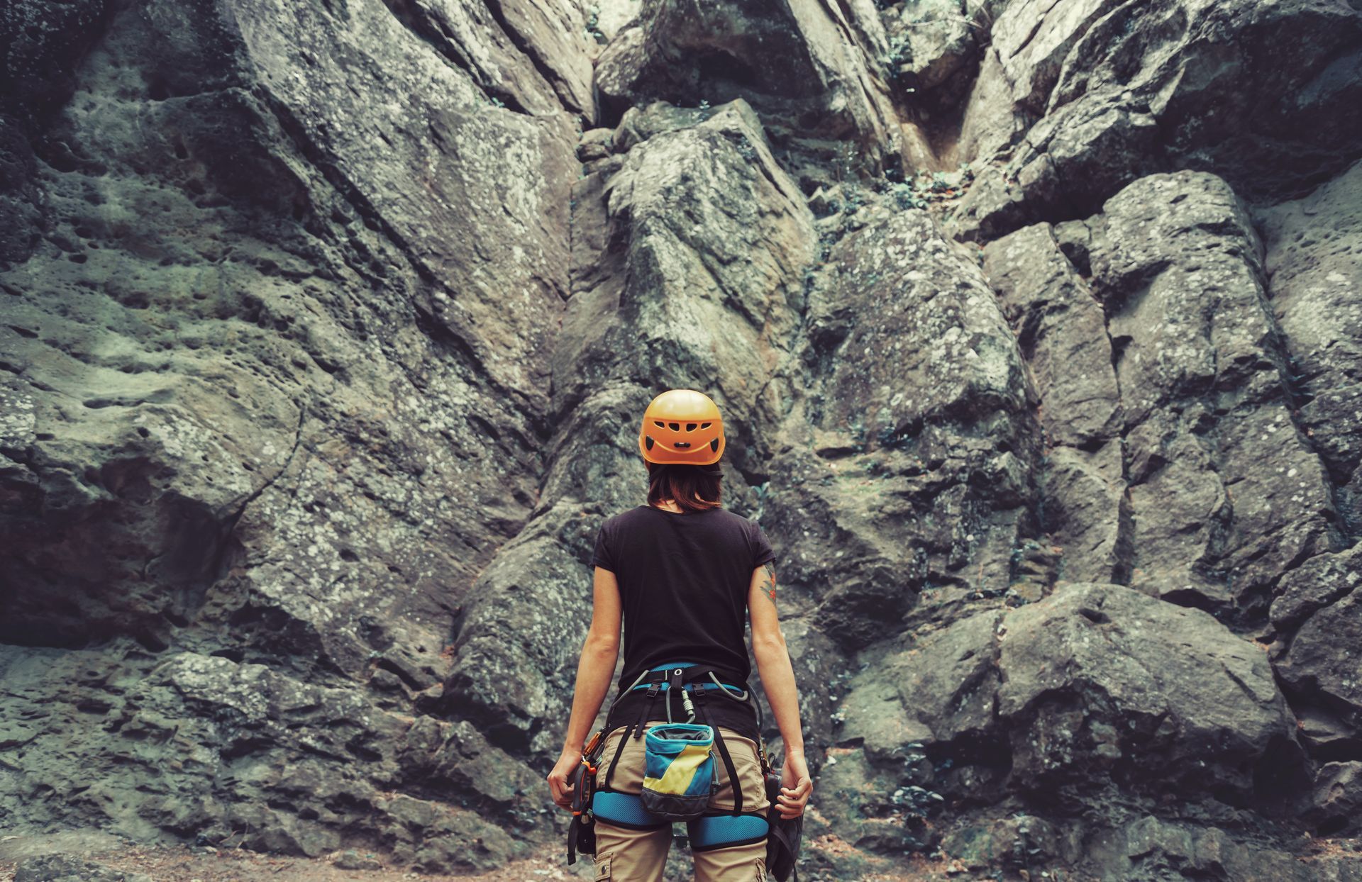 A woman wearing a helmet and a harness is standing in front of a rock wall.