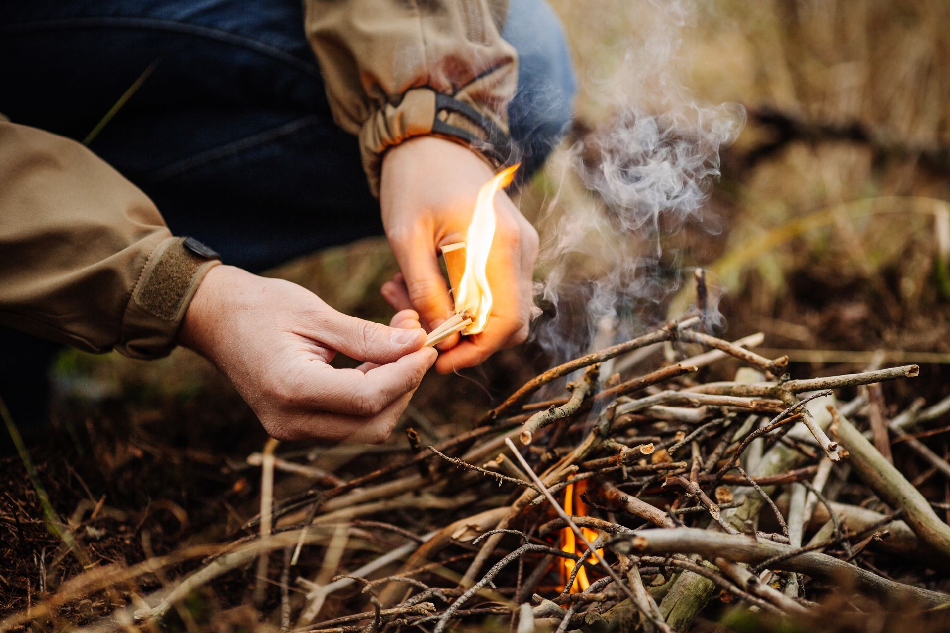 A person is lighting a fire with a match in the woods.