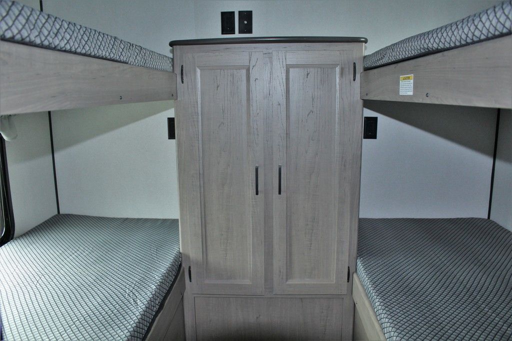 A bunk bed in a trailer with a cabinet and two bunk beds.
