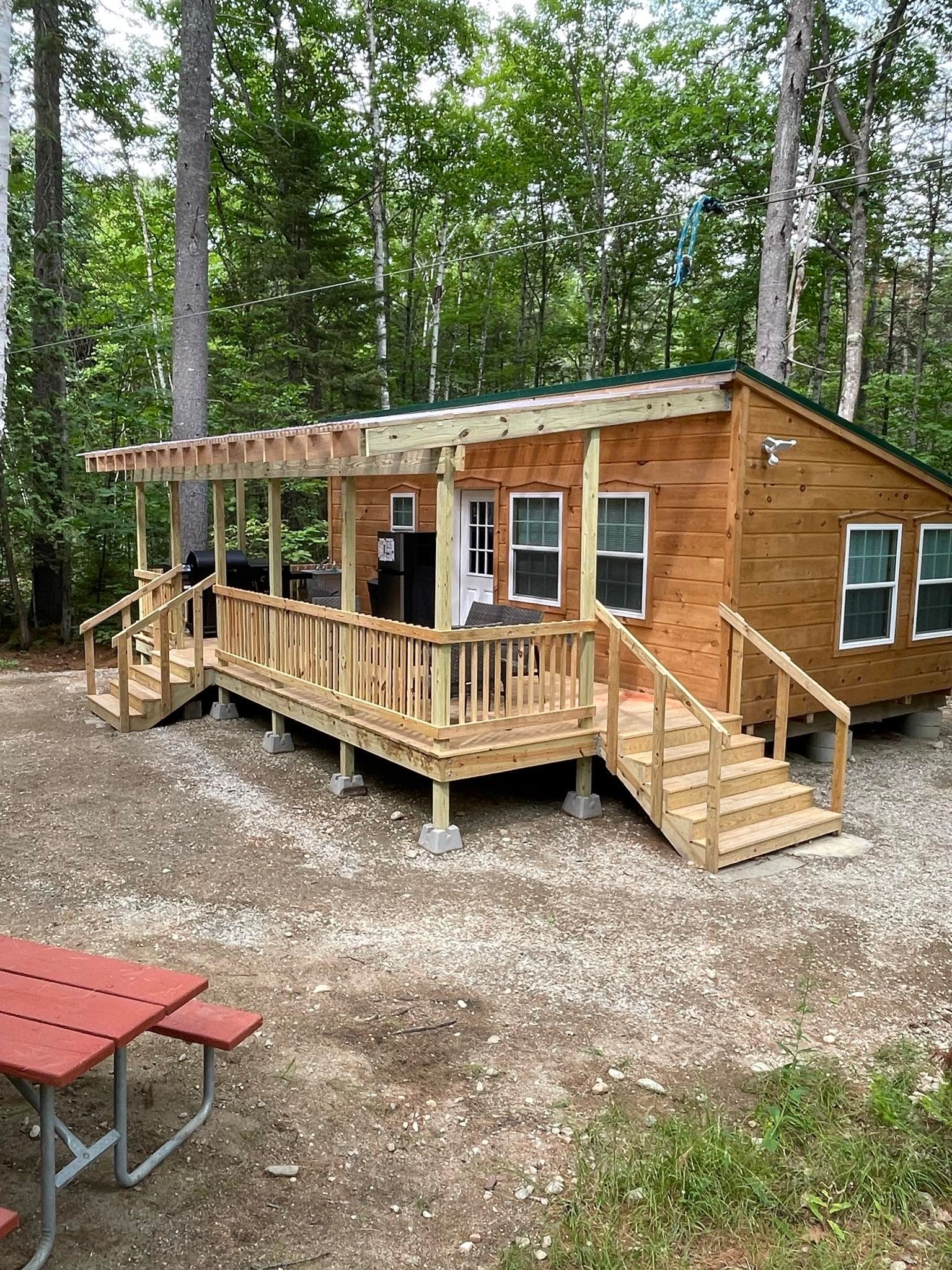 A small wooden cabin with a large deck in the middle of the woods.