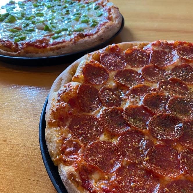 Two pepperoni pizzas are sitting on a wooden table.