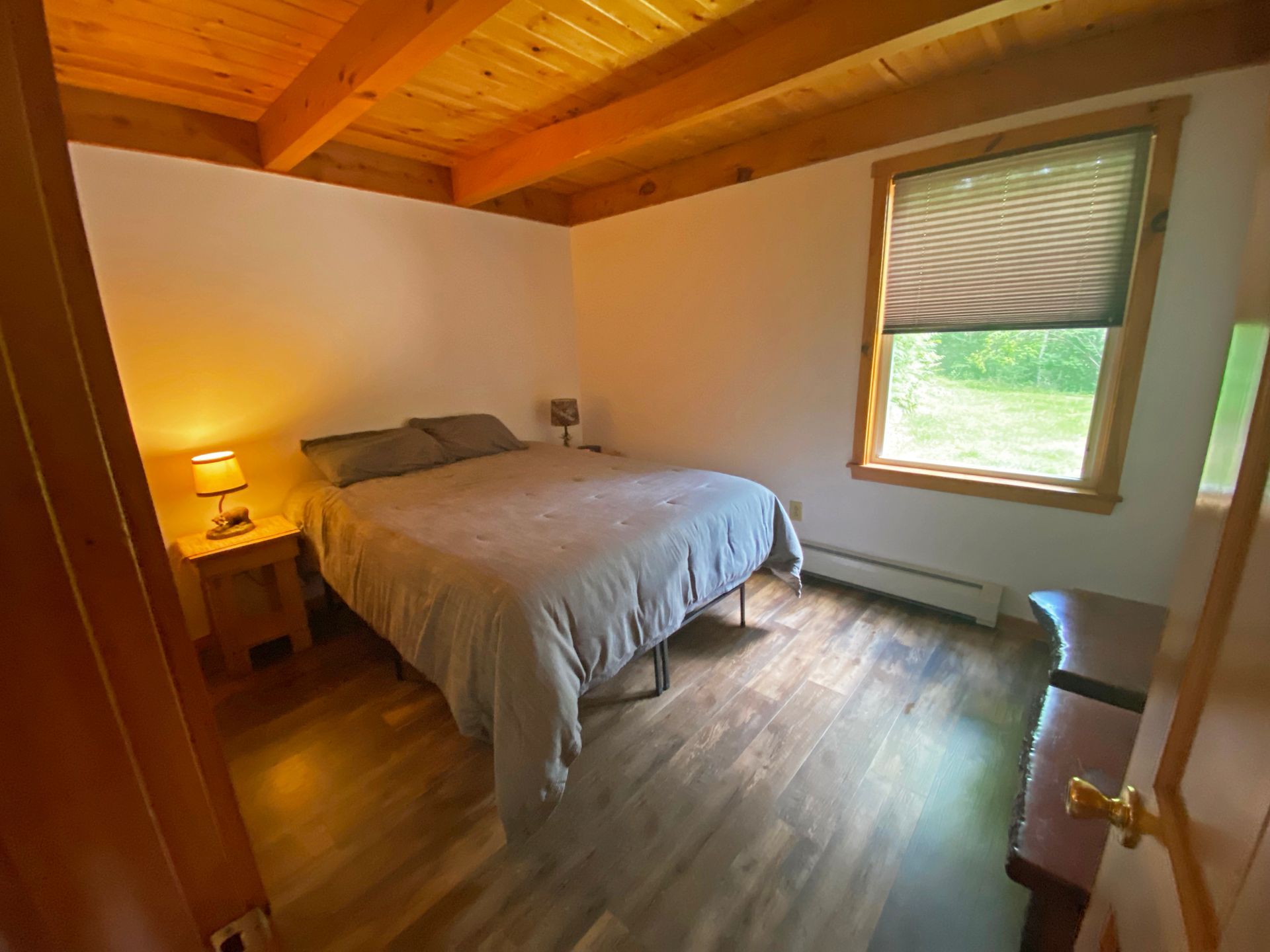A bedroom with a bed , nightstand , lamp and window.
