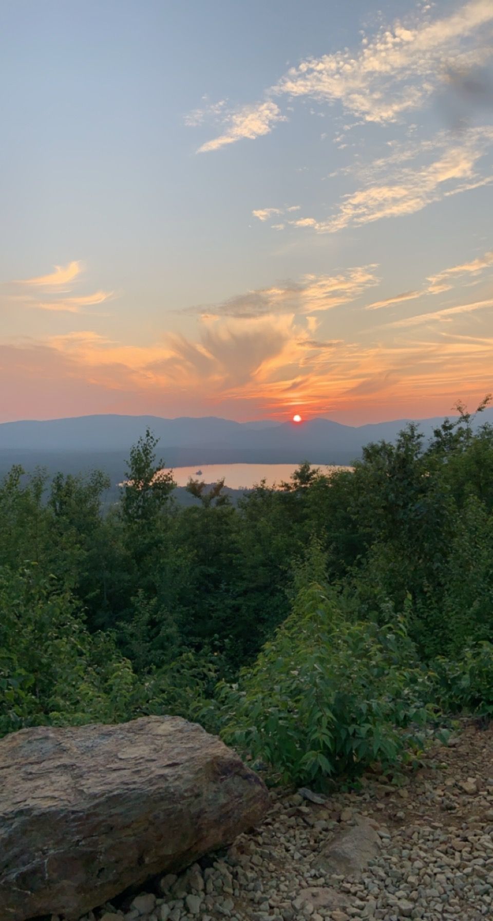 A sunset over a lake with mountains in the background and a rock in the foreground.