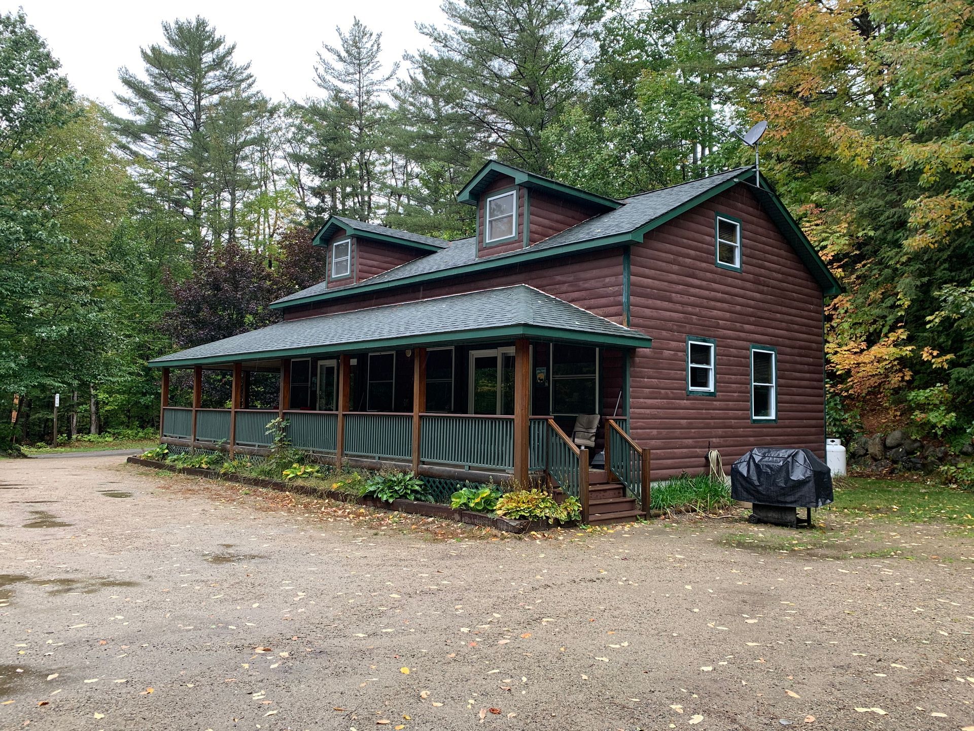 A large wooden house with a large porch in the middle of a forest