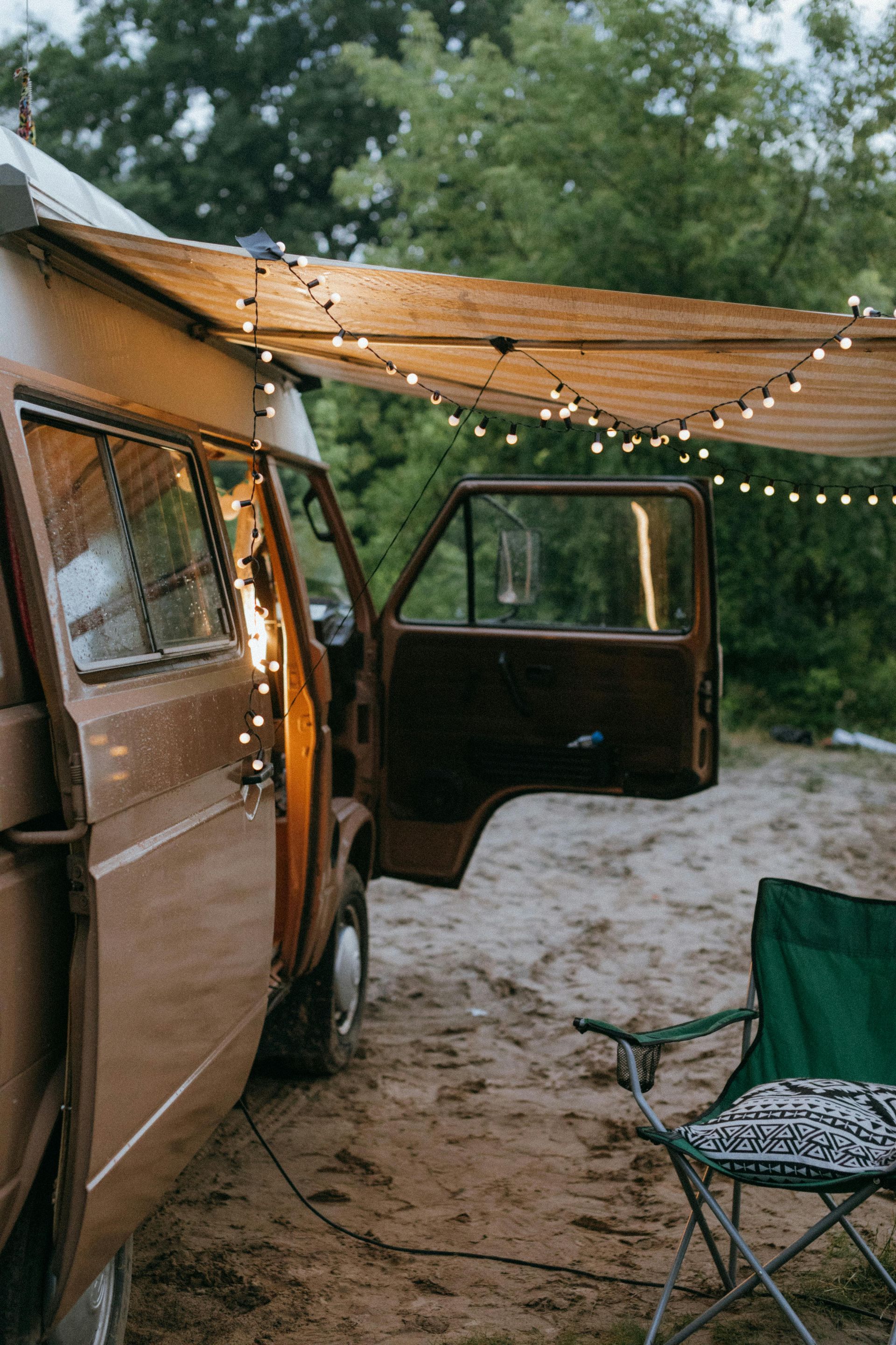 A camper van is parked in the dirt with its door open and a chair.