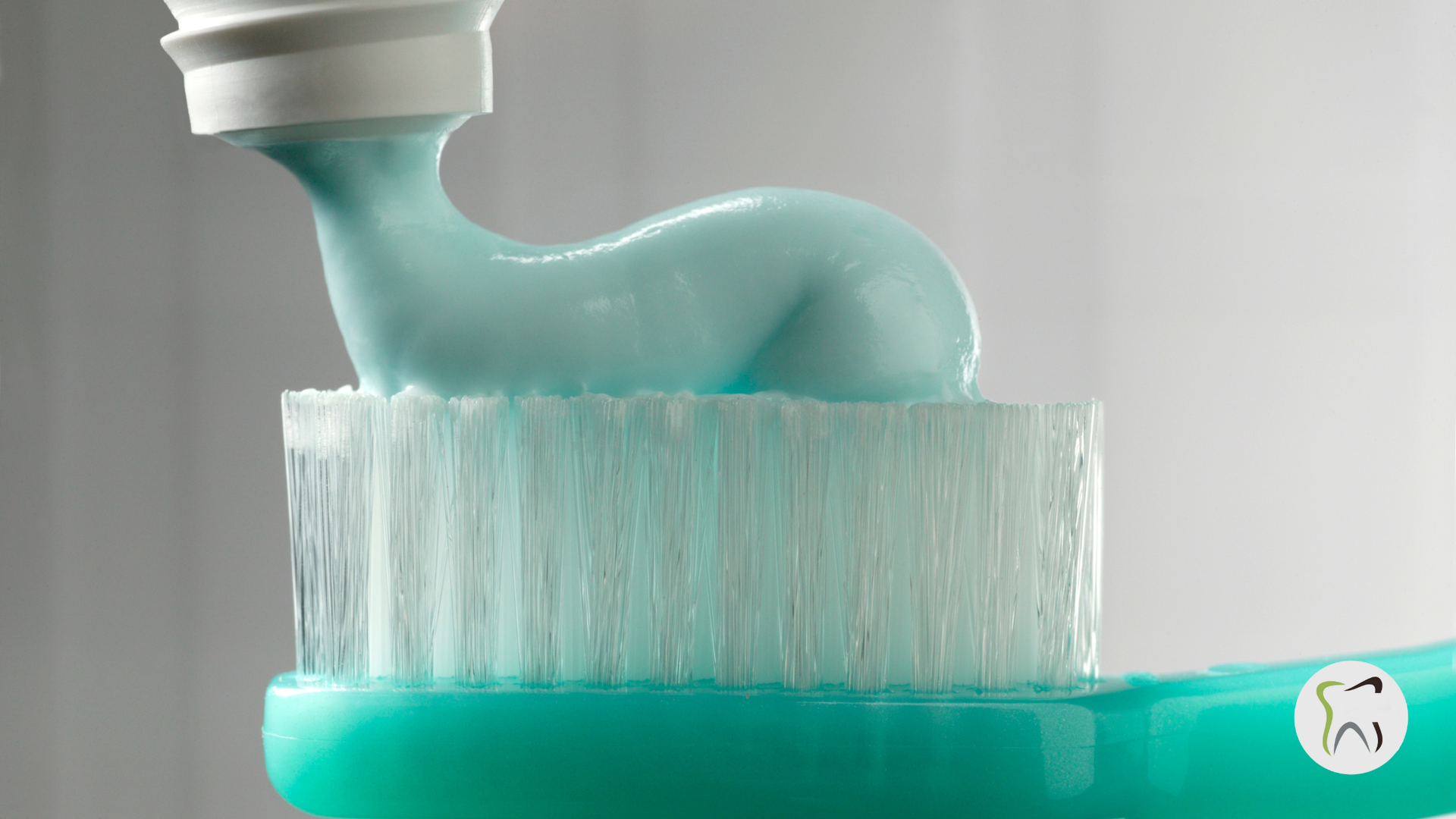Toothpaste being squeezed onto a green toothbrush.