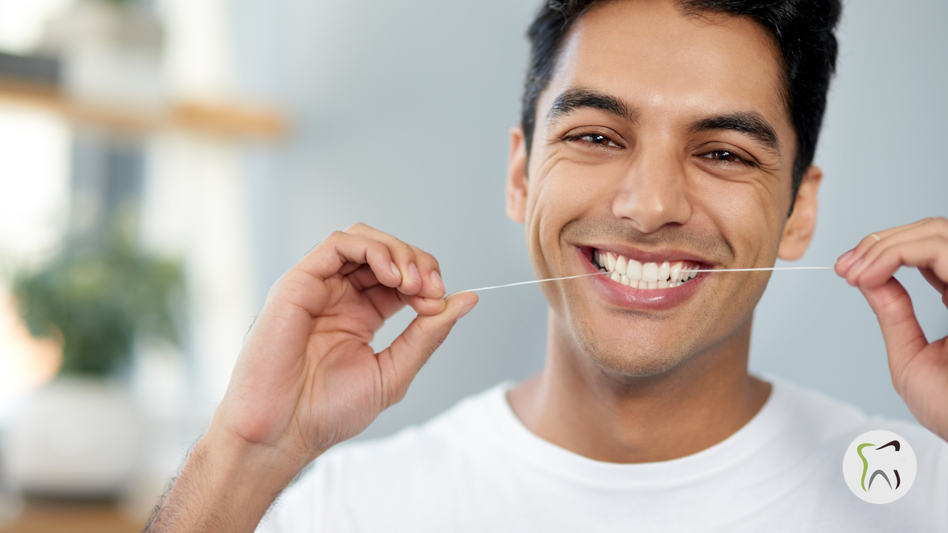 Man smiling, flossing teeth. White shirt, close-up, indoor setting.