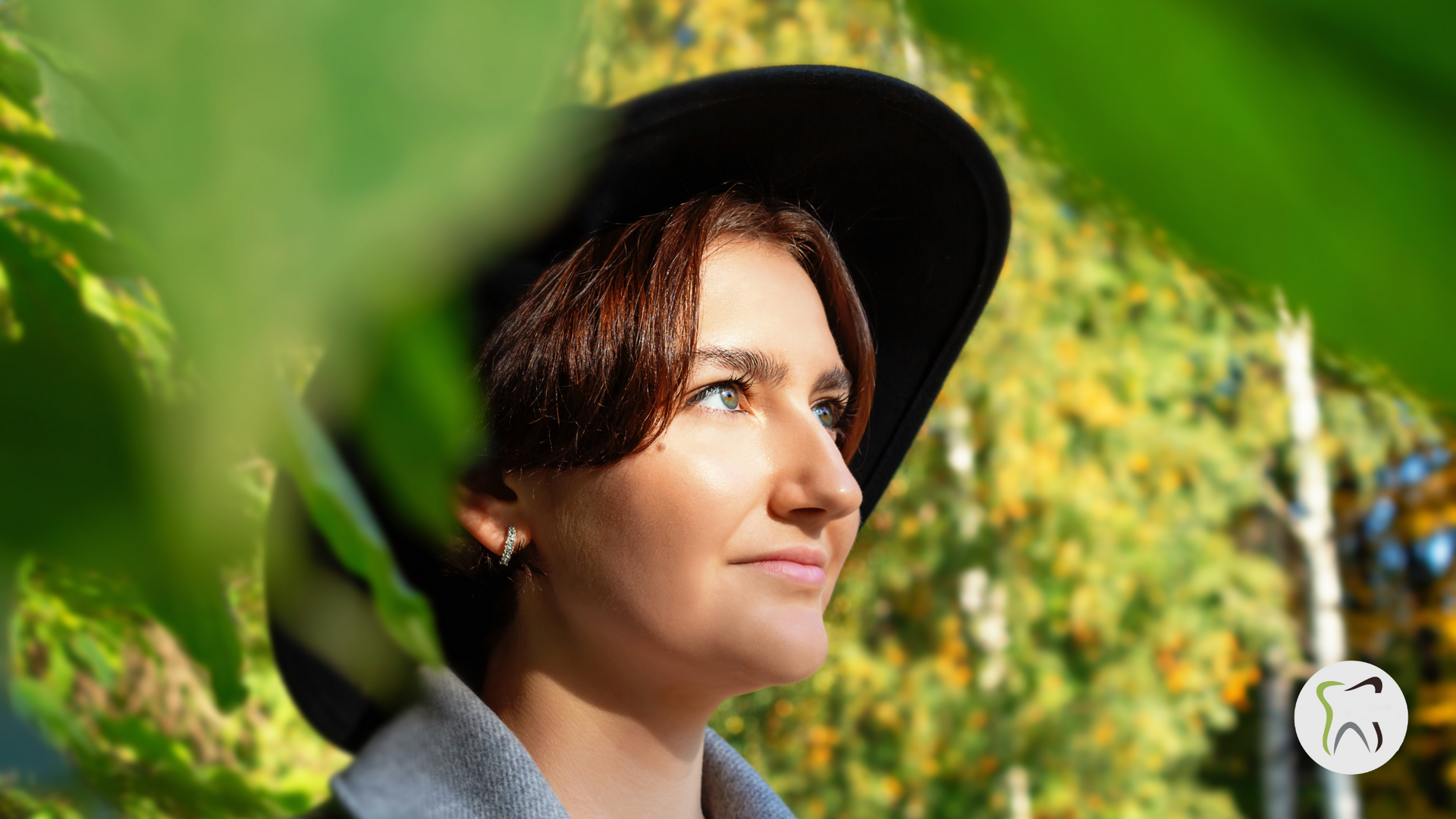 A woman wearing a black hat is standing in front of a tree.