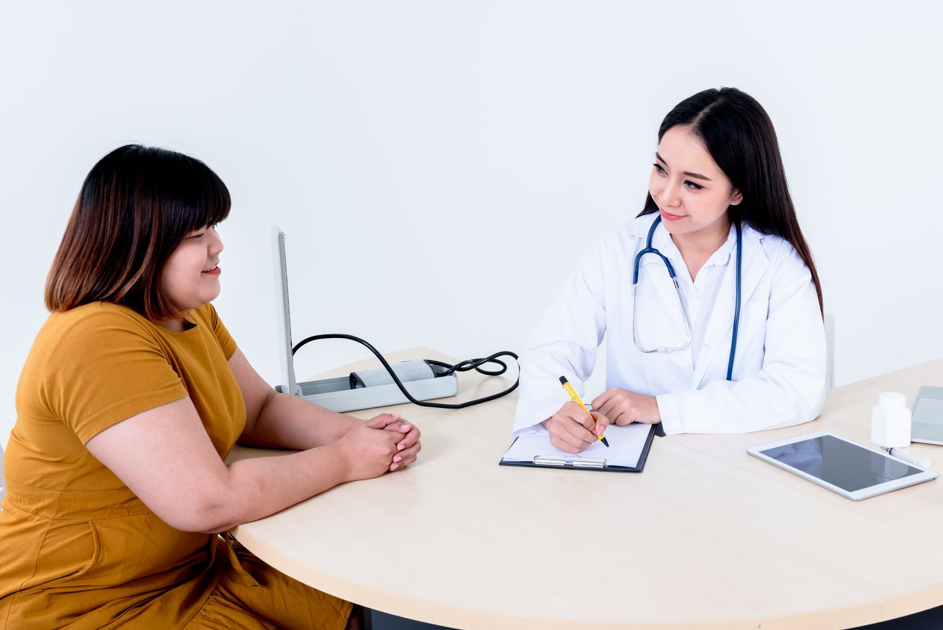 Doctor consulting with a patient at a desk, taking notes in a bright clinic office.