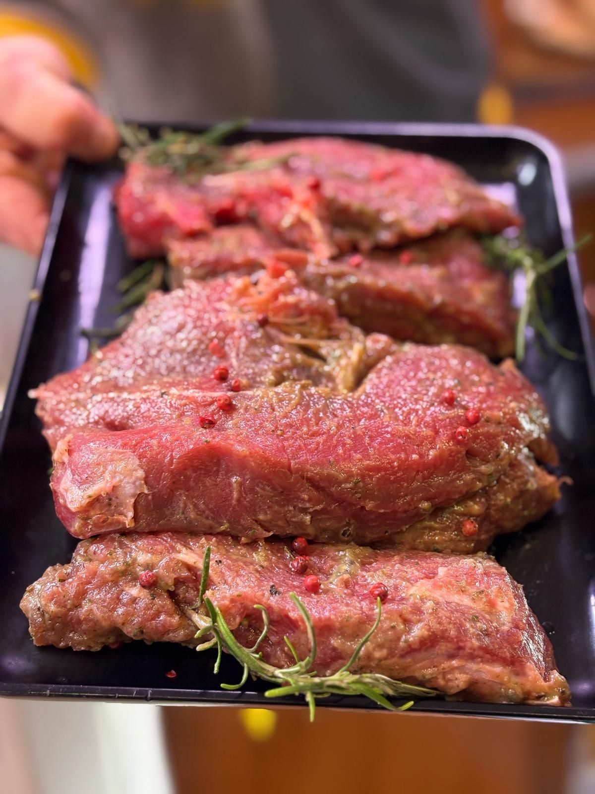 Una persona tiene in mano un vassoio di carne cruda su un tavolo.
