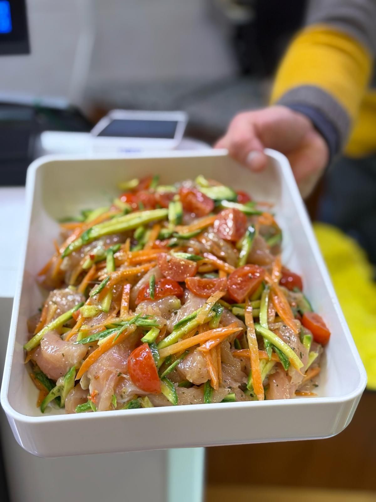 Una persona tiene in mano un vassoio di cibo con pomodori, carote e zucchine.