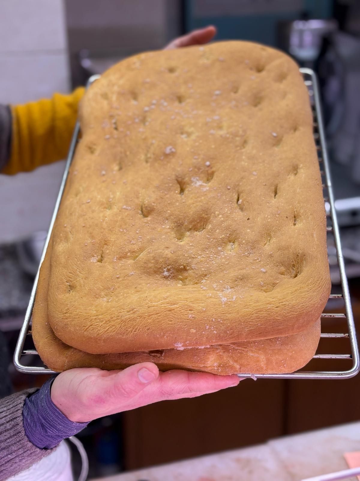 Una persona tiene in mano una pagnotta di pane su una griglia di raffreddamento.