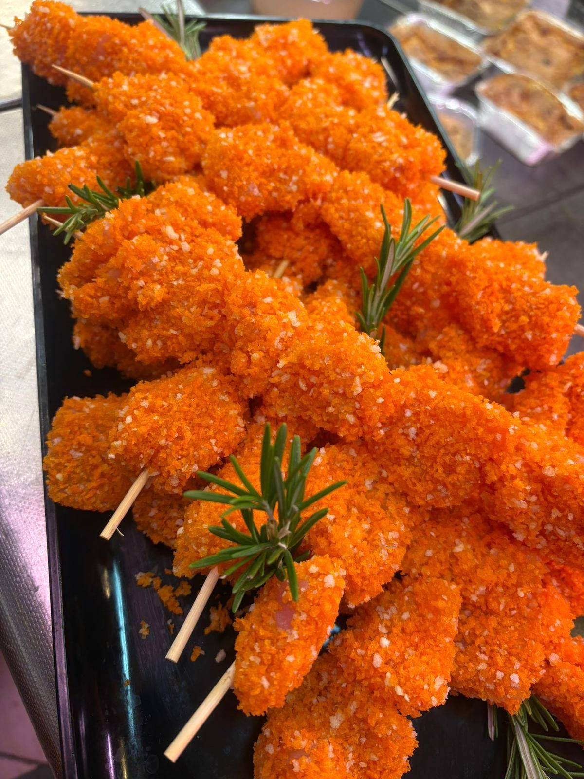 Un vassoio di gamberi fritti su spiedini con rosmarino su un tavolo.
