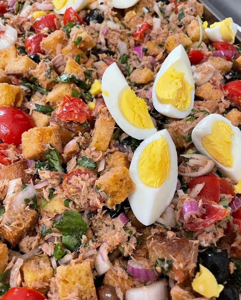 Un primo piano di un'insalata con uova, pomodori, olive e crostini.