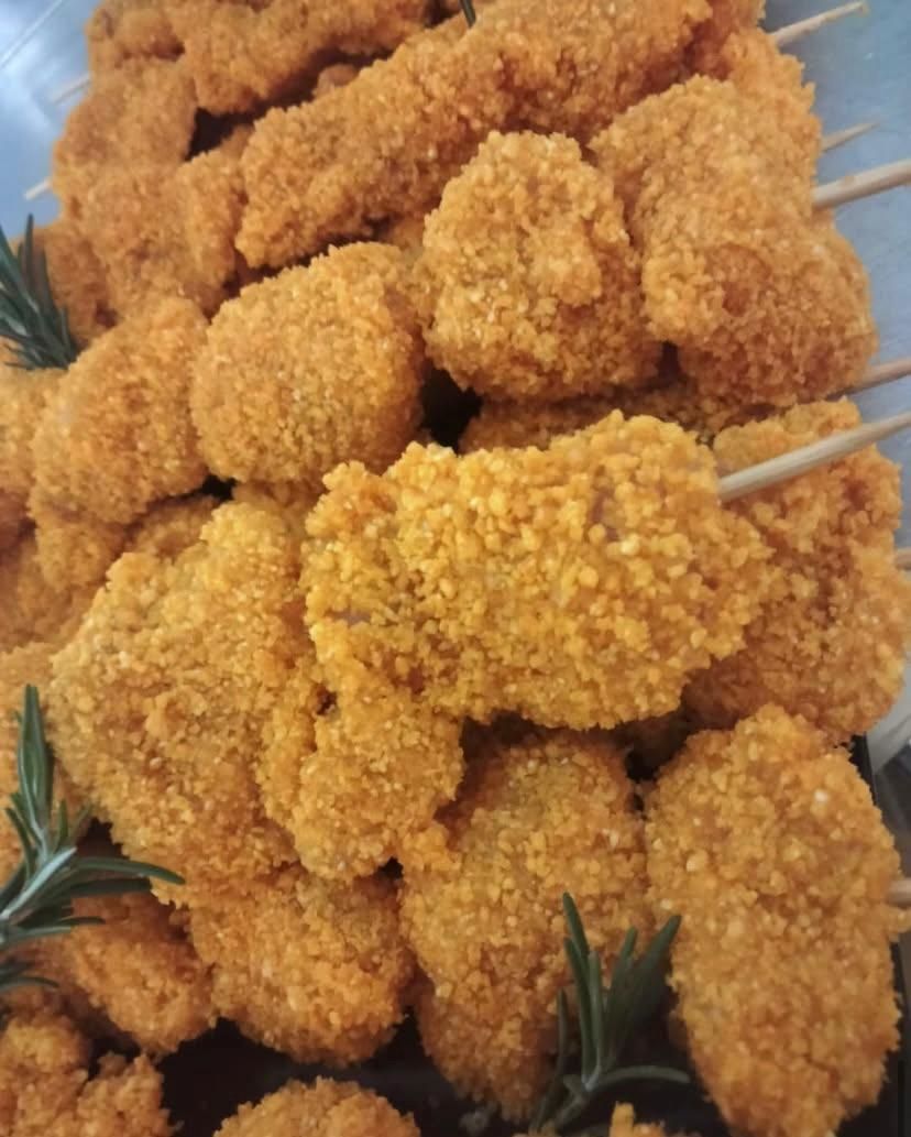 Una pila di bocconcini di pollo infilzati su spiedini con rosmarino sopra.