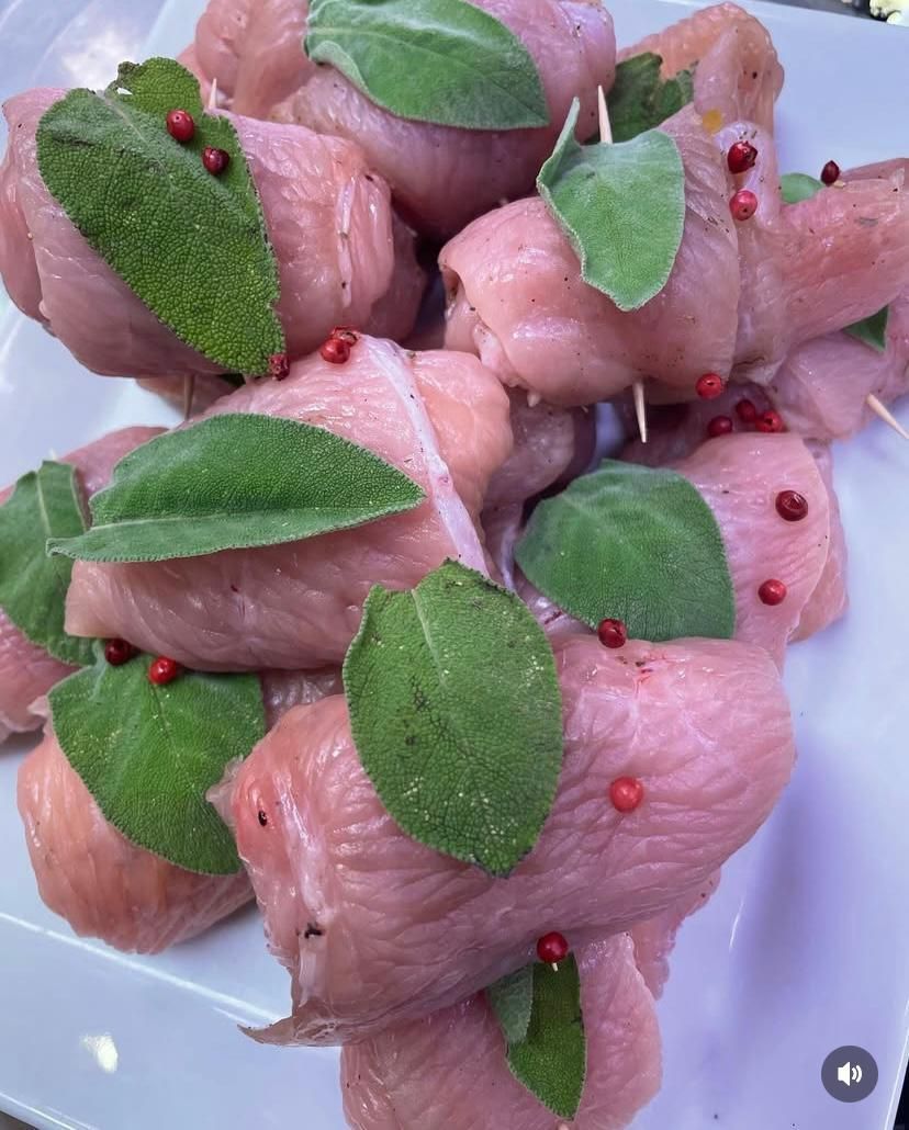 Un piatto bianco con sopra pollo avvolto in salvia e peperoni rossi.