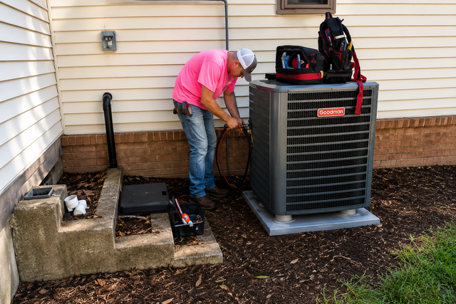 Technician working on an outdoor air conditioner beside a house, with tools and equipment nearby