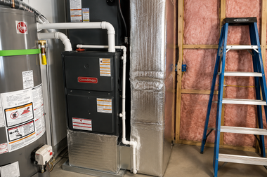 Furnace and water heater in a basement with foil insulation and a blue ladder nearby