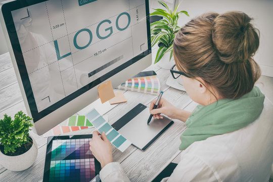 A woman is sitting at a desk working on a logo on a computer.