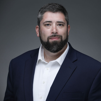 A man with a beard is wearing a suit and smiling.