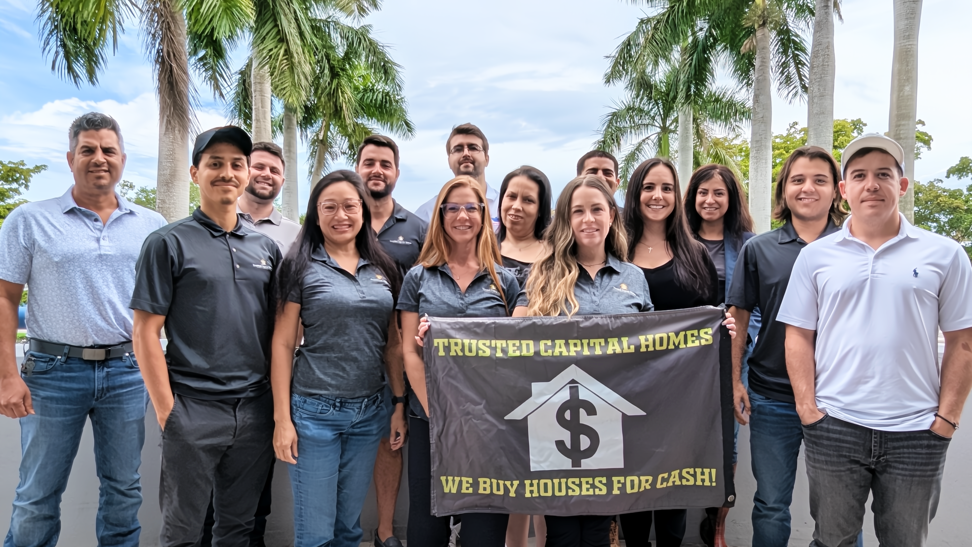 A group of people are posing for a picture while holding a sign that says `` we buy houses for cash ''.
