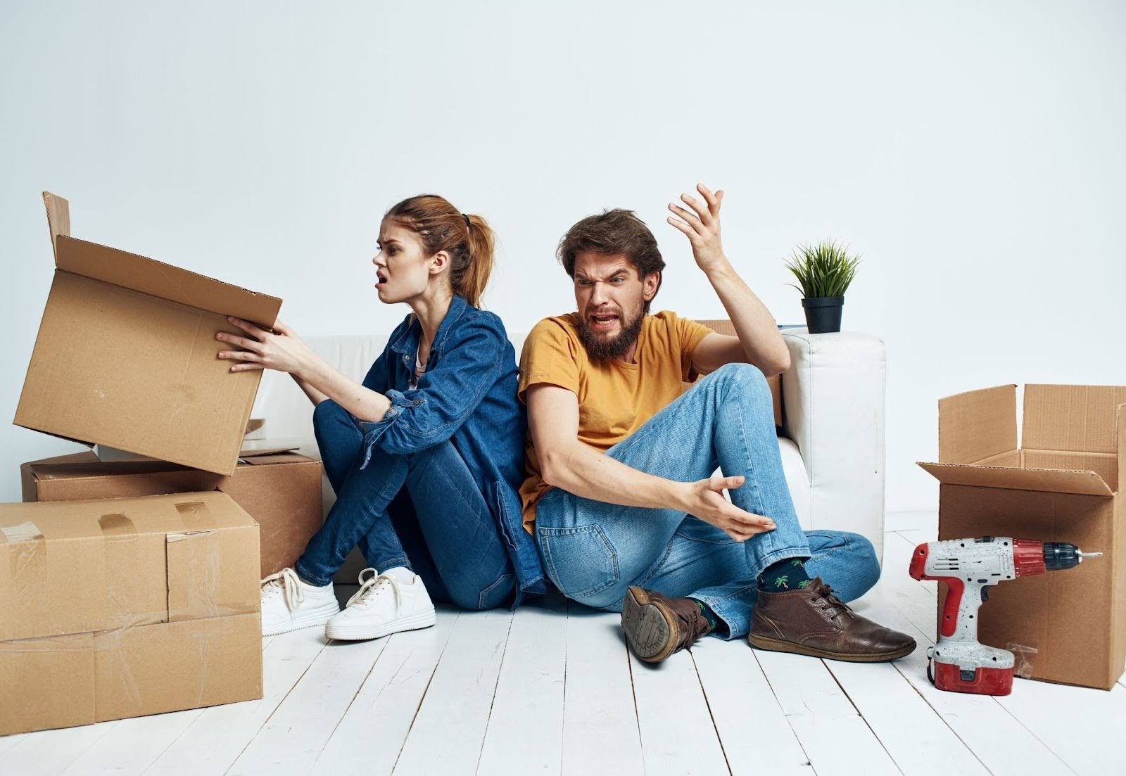 A man and a woman are sitting on the floor surrounded by cardboard boxes.