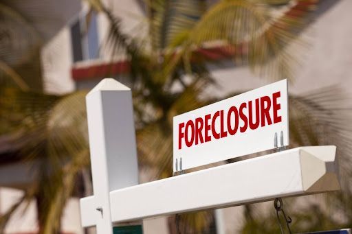 A foreclosure sign is hanging from a fence in front of a building.