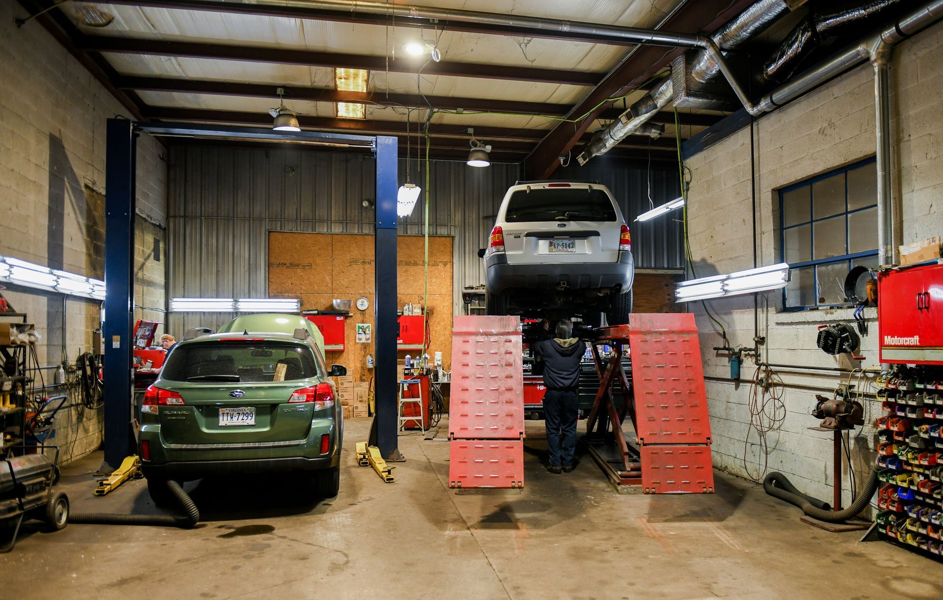 Auto repair shop with two cars on lifts, including a silver SUV raised above red ramps.