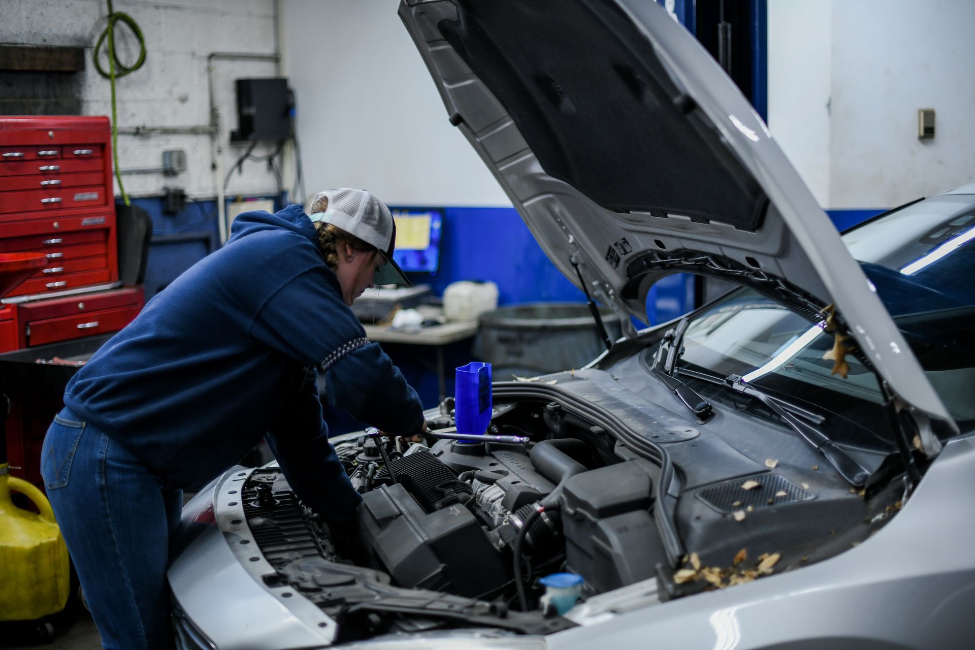 Mechanic working under the hood of a silver car in an auto repair shop