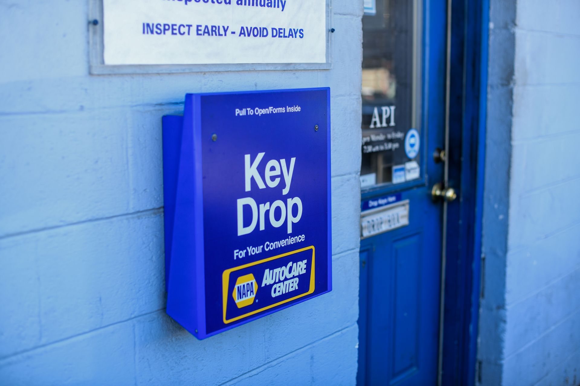 Blue key drop box mounted on a wall next to a door with inspection signs.
